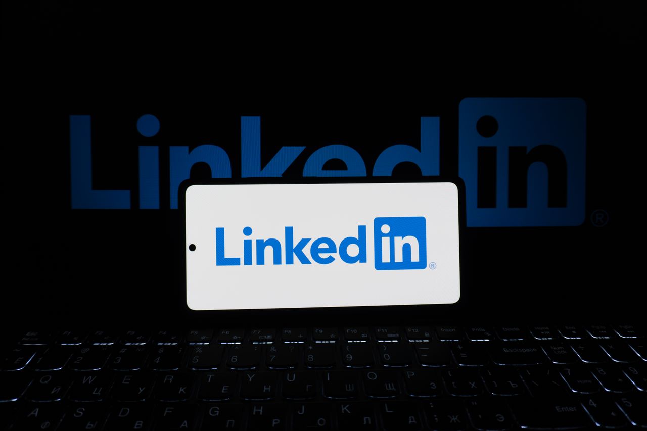 Smartphone displaying the LinkedIn logo with a keyboard and a large logo in the background, business theme.